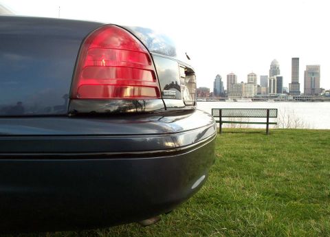 1998 Ford Crown Victoria - Rear view of a dark blue sedan parked on grass with a city skyline across the water.