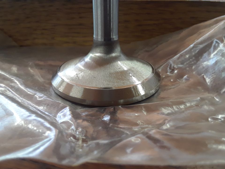 Engine valve with a polished head and stem, resting on plastic wrap