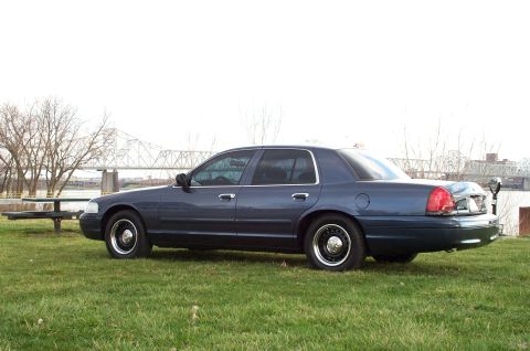 1998 Ford Crown Victoria - This 1998 Ford Crown Victoria is seen from the side, parked on a grassy area with a bridge in the background.