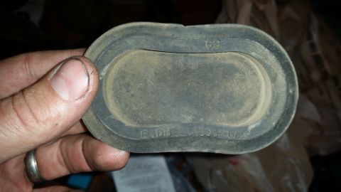 1985 Ford Bronco - A hand holds a dusty, oval-shaped black rubber grommet with embossed text. The grommet appears to be a vehicle part, possibly for a 1985 Fo…