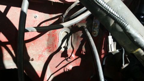 1985 Ford Bronco - This is a close-up view of the engine bay of a red vehicle, showing various hoses, wires, and a grommet on the firewall. Sunlight casts str…