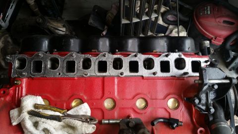 1985 Ford Bronco - A red engine block with a black valve cover and a metal intake manifold gasket is shown. Tools and a white towel are placed on the engine b…
