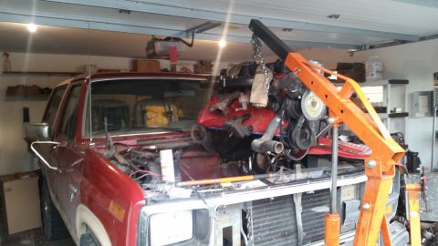 1985 Ford Bronco - A red Ford Bronco is in a garage with its engine removed and suspended by an engine hoist.