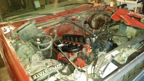 1985 Ford Bronco - The engine bay of a red vehicle, an Interstate battery and various engine components.