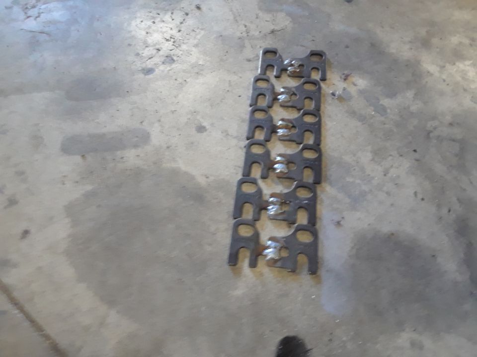 Row of metal brackets with holes, laid out on a concrete floor