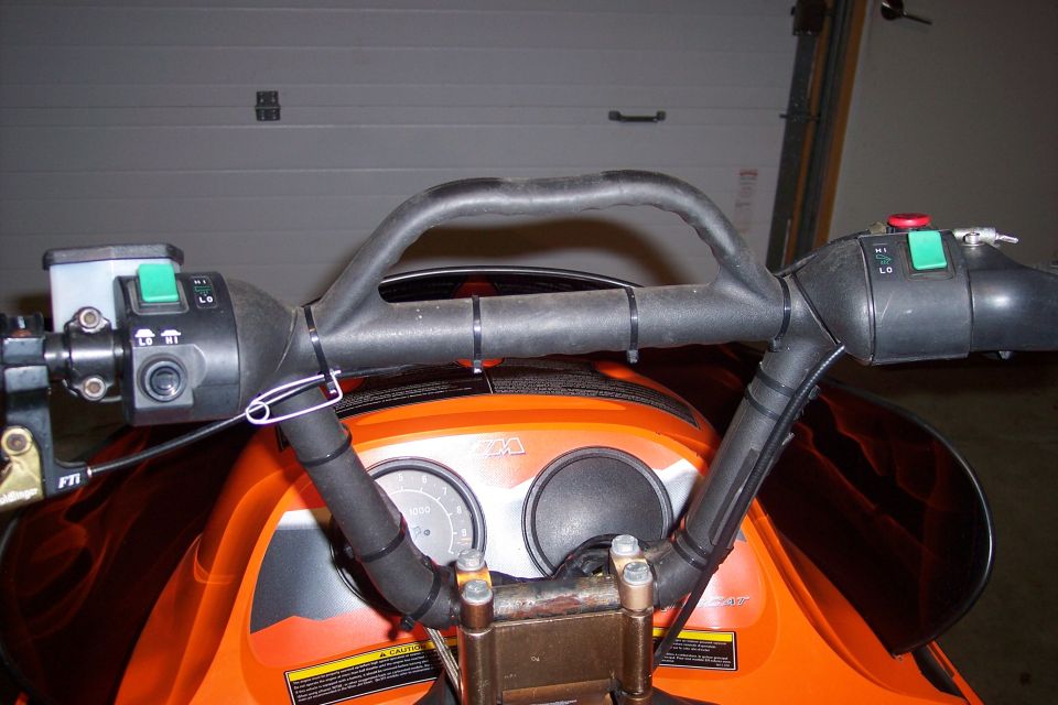 Orange snowmobile handlebars with black grips and controls, showing two gauges and a safety pin
