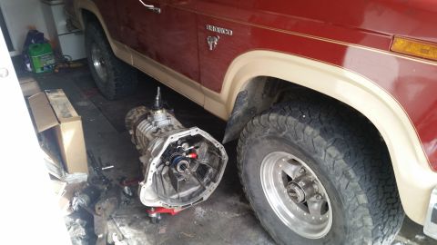1985 Ford Bronco - A red and tan Ford Bronco is parked next to a removed transmission in a garage.