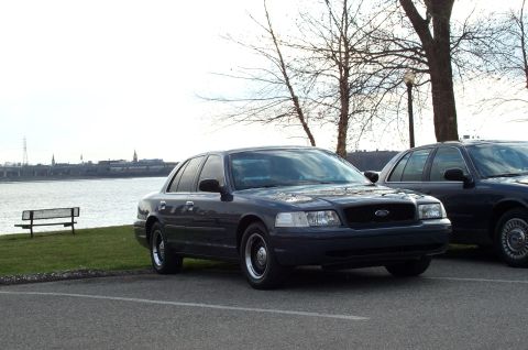 1998 Ford Crown Victoria - A 1998 Ford Crown Victoria is parked near a waterfront, with another vehicle partially visible behind it.