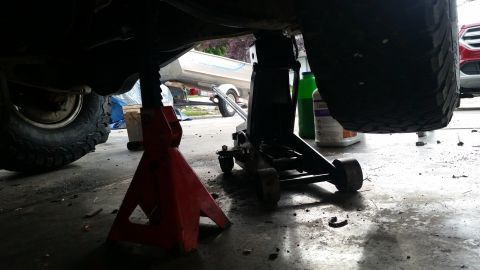 1985 Ford Bronco - The vehicle is supported by jack stands and a floor jack, indicating it is undergoing maintenance or repair.