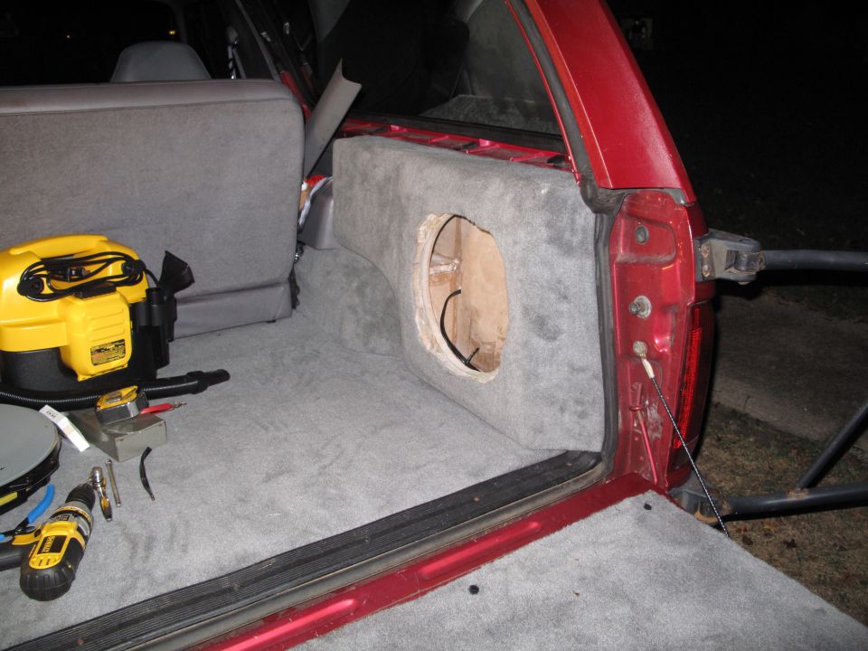 red SUV interior with carpeted subwoofer box being installed, tools and shop vac nearby