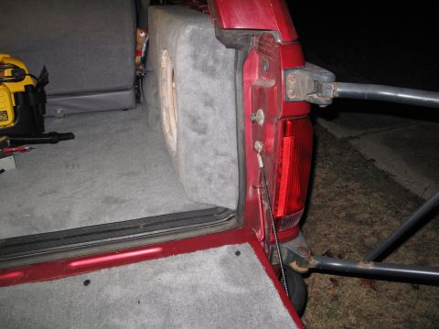 1994 Ford Bronco - The rear interior of a red SUV shows a custom subwoofer box and gray carpeting, with a yellow power tool visible.