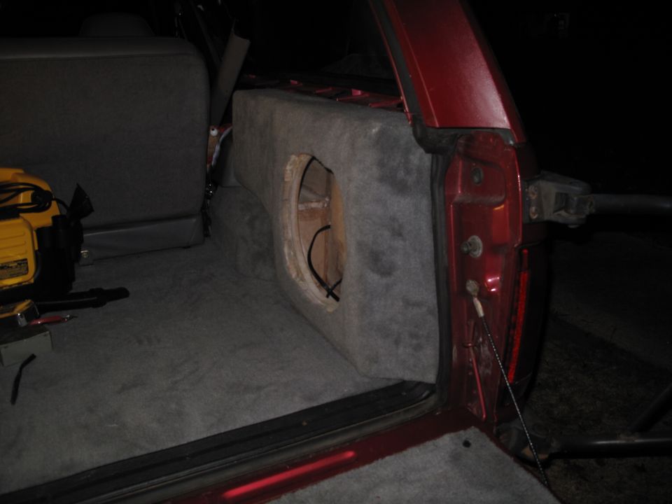 Red SUV interior with custom subwoofer box and yellow power tool. Rear door open