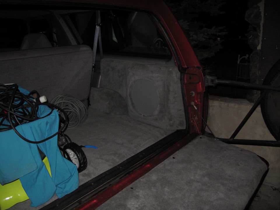 Red SUV interior cargo area with custom subwoofer box and coiled cables