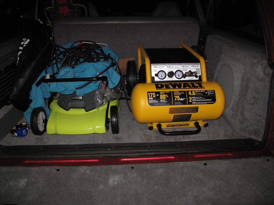 Ryobi lawn mower and yellow DeWalt air compressor loaded in cargo area of a vehicle