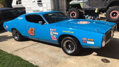 1971 Dodge Charger - A blue 1971 Dodge Charger with racing decals is parked outside, with a trailer and a lifted Jeep in the background.