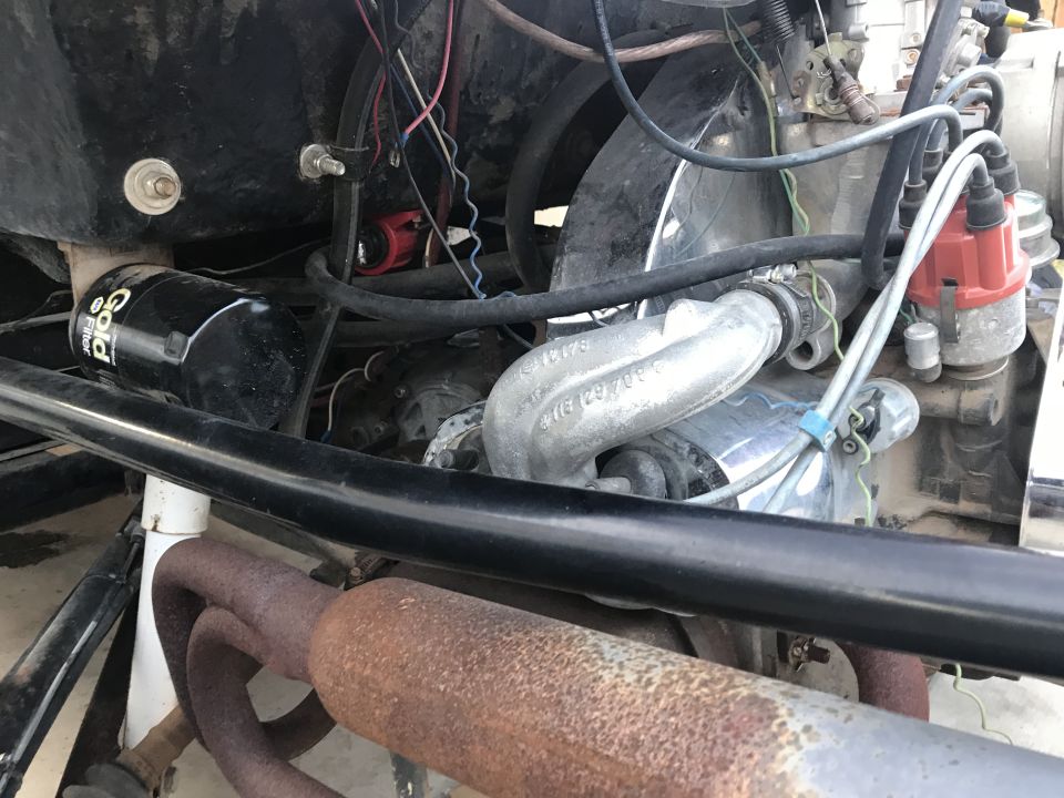 Close-up of a Volkswagen Beetle engine bay, showing the oil filter, distributor, and exhaust pipes