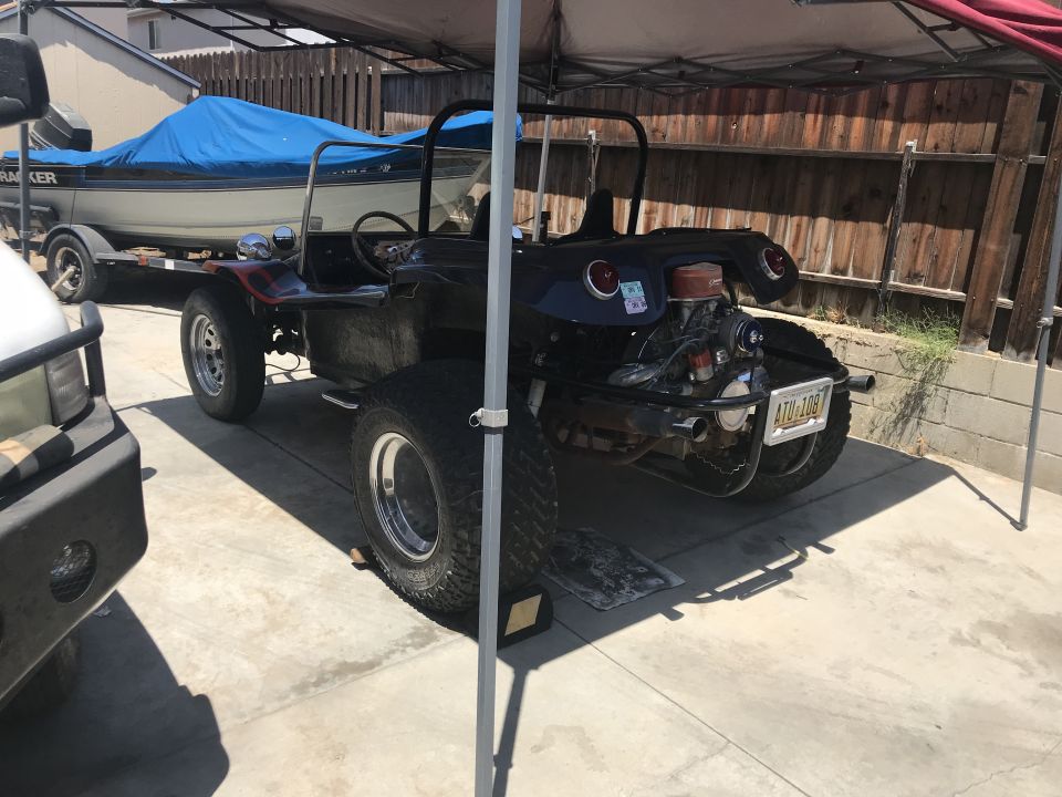 Black dune buggy with exposed engine and large rear tires, parked under a canopy
