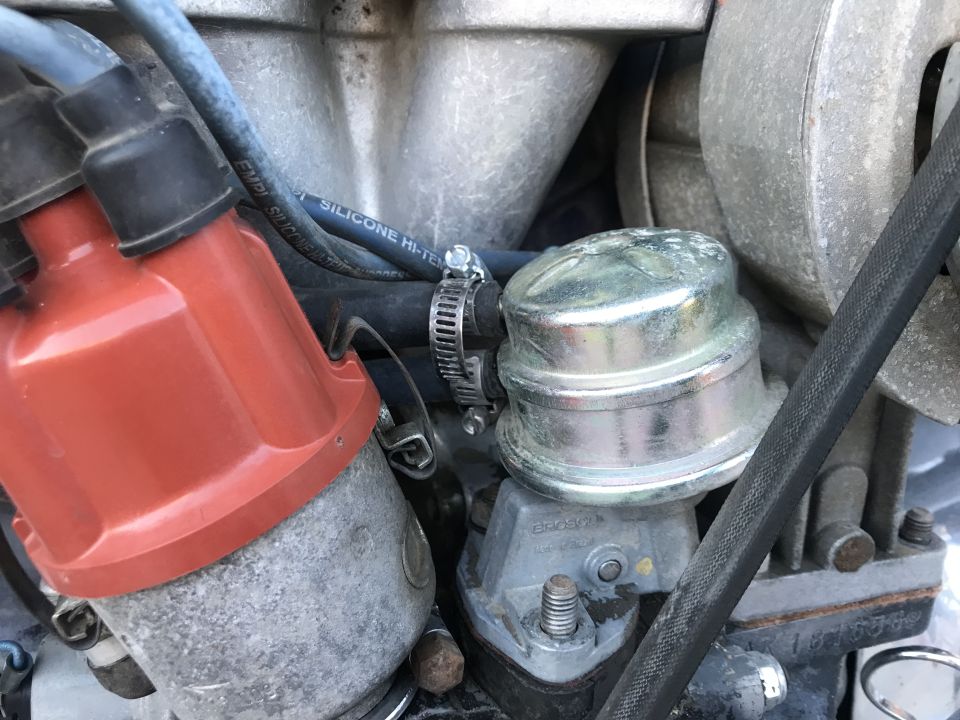 Close-up of VW Beetle engine parts: red distributor cap, fuel pump, blue hose with text, black belt.