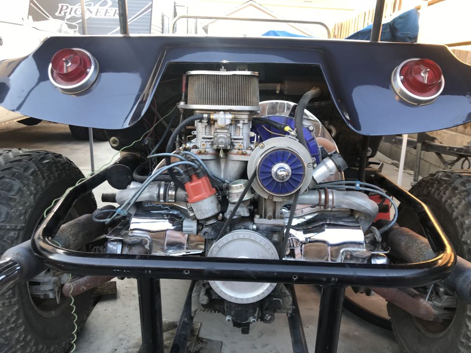 Rear view of a dark blue dune buggy with exposed engine and large off-road tires.