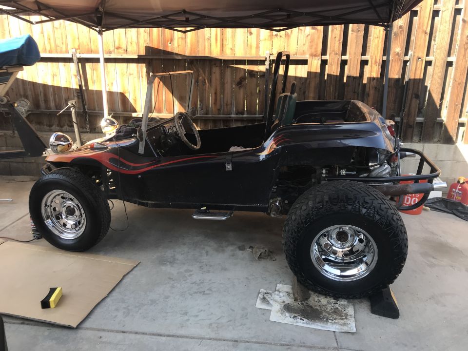 Black dune buggy with flame graphics, large tires, and chrome wheels, parked outdoors.