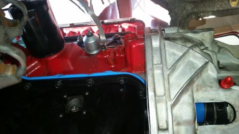 1985 Ford Bronco - A close-up view shows the engine block of a vehicle, painted red, with a black oil pan attached by bolts and a blue gasket. A silver oil fi…
