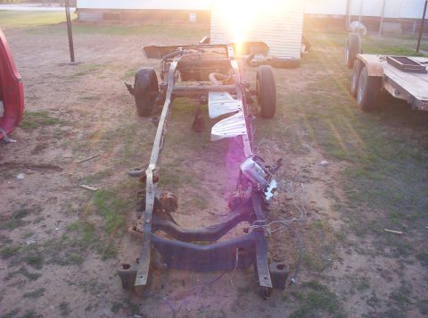 1988 Ford Bronco - The chassis of a vehicle sits in a yard, with a trailer visible in the background.