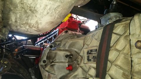 1985 Ford Bronco - A close-up view of a Ford transmission housing with a red plug and a black and red strap. The transmission has a "Ford" logo and a label wi…
