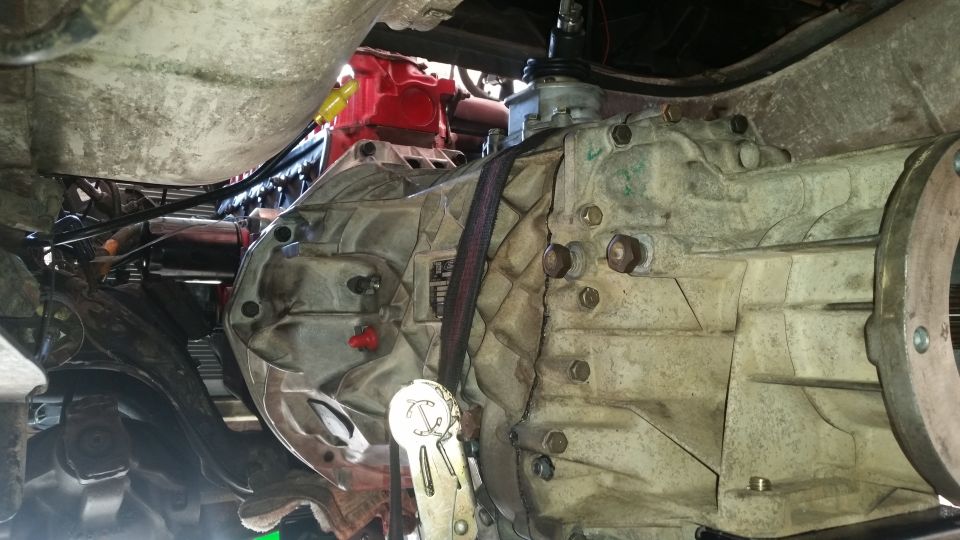 Underside of a vehicle showing a large aluminum transmission housing secured with a strap.