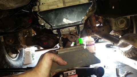 1985 Ford Bronco - A person's hand holds a metal bracket underneath a vehicle's transmission or transfer case. The bracket appears to be part of a mount or su…