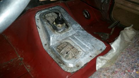 1985 Ford Bronco - The interior of a vehicle shows a close-up of the center console area, focusing on the gear shifter and the surrounding metal and red floor…