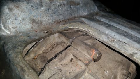 1985 Ford Bronco - A close-up view shows a cracked metal casing, likely part of a vehicle's transmission or drivetrain, with visible black sealant or residue…