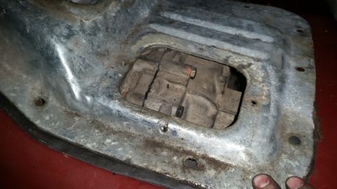 1985 Ford Bronco - A close-up view of a vehicle's transmission housing and a metal underbody shield, seen from a low angle.