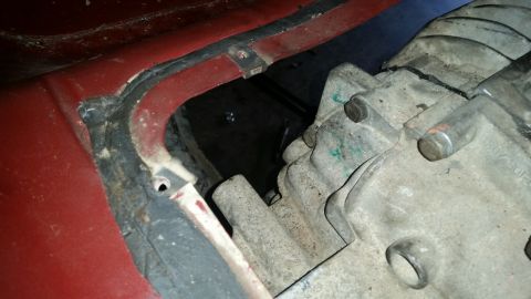 1985 Ford Bronco - A close-up view shows a portion of a red vehicle body with a black rubber seal. Adjacent to the body is a dirty, gray metal component, like…