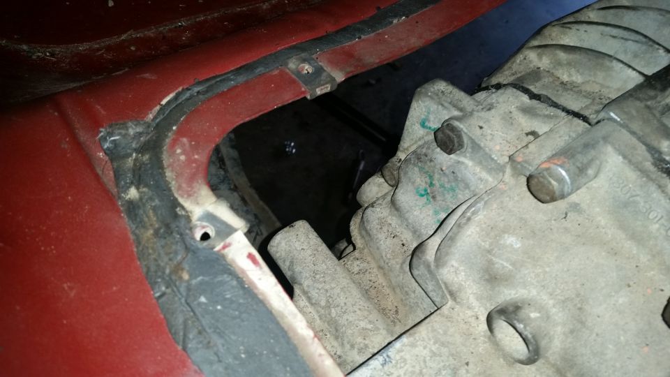 Close-up of red vehicle body with black seal next to a dirty gray engine/transmission part.