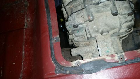 1985 Ford Bronco - A close-up view shows the transmission housing of a vehicle, partially obscured by a red painted metal panel with black sealant. The transm…