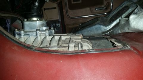 1985 Ford Bronco - Close-up view of a transfer case mounted between the seats of a vehicle, likely a truck or SUV. The transfer case is silver and appears to…