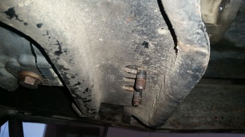 1985 Ford Bronco - This image shows the underside of a vehicle, focusing on a heavily corroded metal component with two bolts protruding. A hexagonal bolt hea…