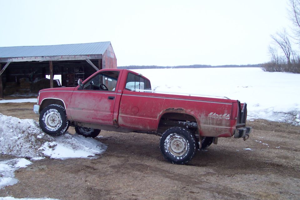 Red single-cab Chevrolet 4x4 pickup parked by a barn in a snowy rural setting