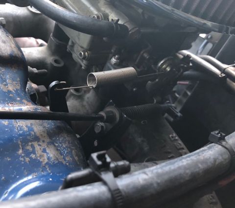 1981 Ford Bronco - A close-up view of the throttle linkage and return spring on a carburetor, likely from a 1981 Ford Bronco. The blue painted engine componen…