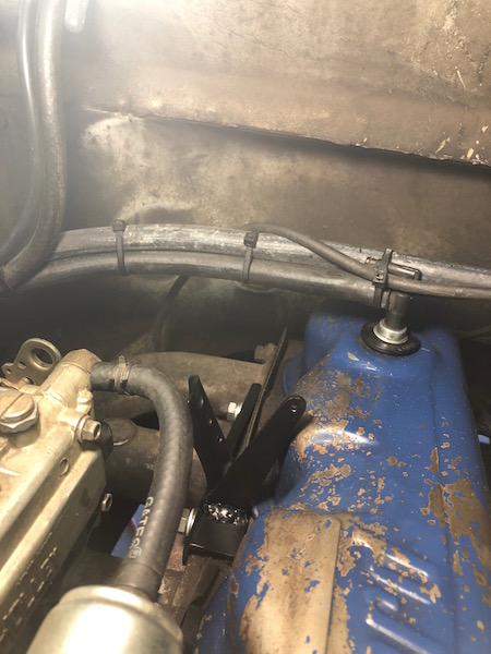 1981 Ford Bronco - A close-up view of a black metal bracket installed on the engine of a vehicle. The bracket is attached to the blue valve cover and appears…
