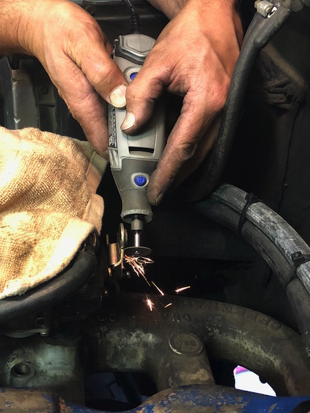 1981 Ford Bronco - A person is using a Dremel tool with a cutting wheel to cut a metal part on what appears to be an engine. Sparks are flying from the point…