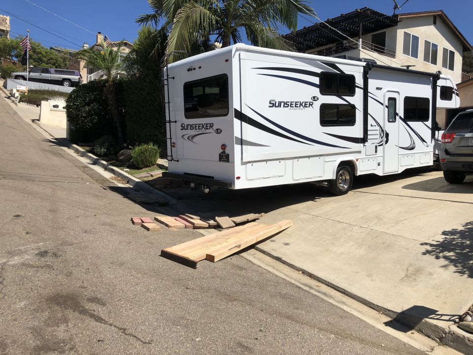 White Sunseeker RV parked on a sloped driveway with wooden planks and bricks on the ground.
