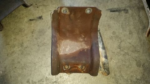 1985 Ford Bronco - A heavily rusted metal bracket with two sets of bolt holes is shown lying on a concrete floor. The bracket appears to be a vehicle part, po…