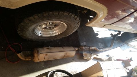 1985 Ford Bronco - The underside of a vehicle shows a large exhaust muffler and pipe assembly, along with a tire and wheel. The vehicle appears to be a truck…
