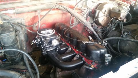 1985 Ford Bronco - The image shows a close-up view of the engine bay of a vehicle, focusing on the carburetor and intake manifold. The engine components are b…