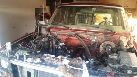 1985 Ford Bronco - Red SUV's engine bay is open for work, showing disassembled components and tools.