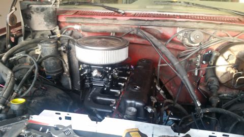 1985 Ford Bronco - The image shows a close-up view of a red Ford Bronco's engine bay, focusing on the carburetor and air intake assembly. Various hoses, wires…