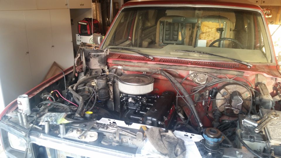 Engine bay of a red Ford Bronco with engine, air filter, tools, and a soda can visible.
