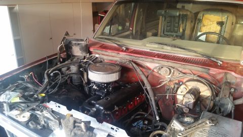 1985 Ford Bronco - The engine bay of a red Ford Bronco is shown with the engine partially disassembled. Tools are laid out on the front of the vehicle, sugges…