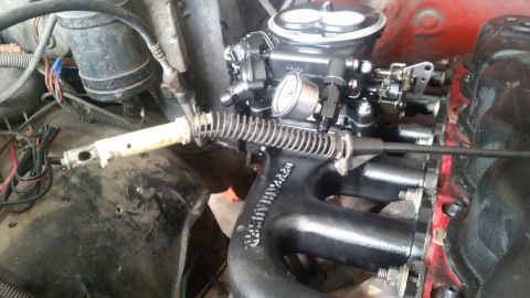 1985 Ford Bronco - A close-up view of a Holley carburetor and intake manifold on a V8 engine. A throttle cable assembly with a return spring is visible, along…